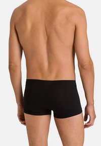 Černé boxerky s hladkou texturou, středním pasem a minimem švů, viděné zezadu na jednoduchém pozadí.
