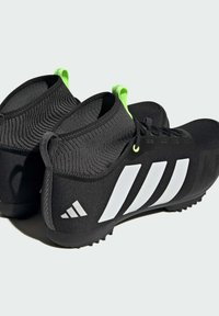 Chaussures de sport noires avec une tige en tricot, présentant un bout arrondi, trois rayures blanches sur le côté et des accents verts sur la languette au talon.