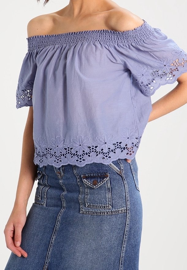 Femme portant un haut lavande épaules dénudées avec une bordure en dentelle florale et une jupe en denim bleu taille haute avec poches avant.