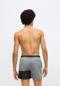 Szürke és fekete úszónadrág elasztikus derékpánttal, két zsebbel és egy logóval a hátsó részen. Az anyag könnyűnek és gyorsan száradónak tűnik.