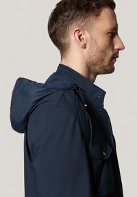 Granatowa kurtka z kapturem z zamkiem z przodu, regulowanym kapturem na sznurku i wieloma kieszeniami. Gładka tekstura z prostym designem.