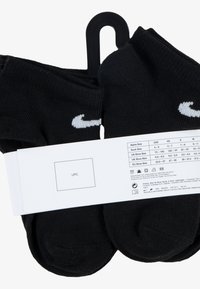 Čierne ponožky zo zmesi bavlny s bielym logom Nike, zabalené s bielou etiketou zobrazujúcou veľkosť a pokyny na starostlivosť. Hladká textúra, dĺžka po členky.