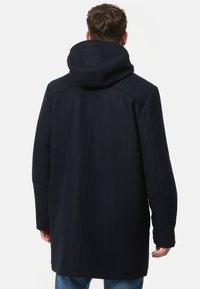 Marineblauwe wollen jas met een grote capuchon, lange mouwen en een rechte snit. Voorzien van zichtbare naden en een minimalistisch ontwerp.