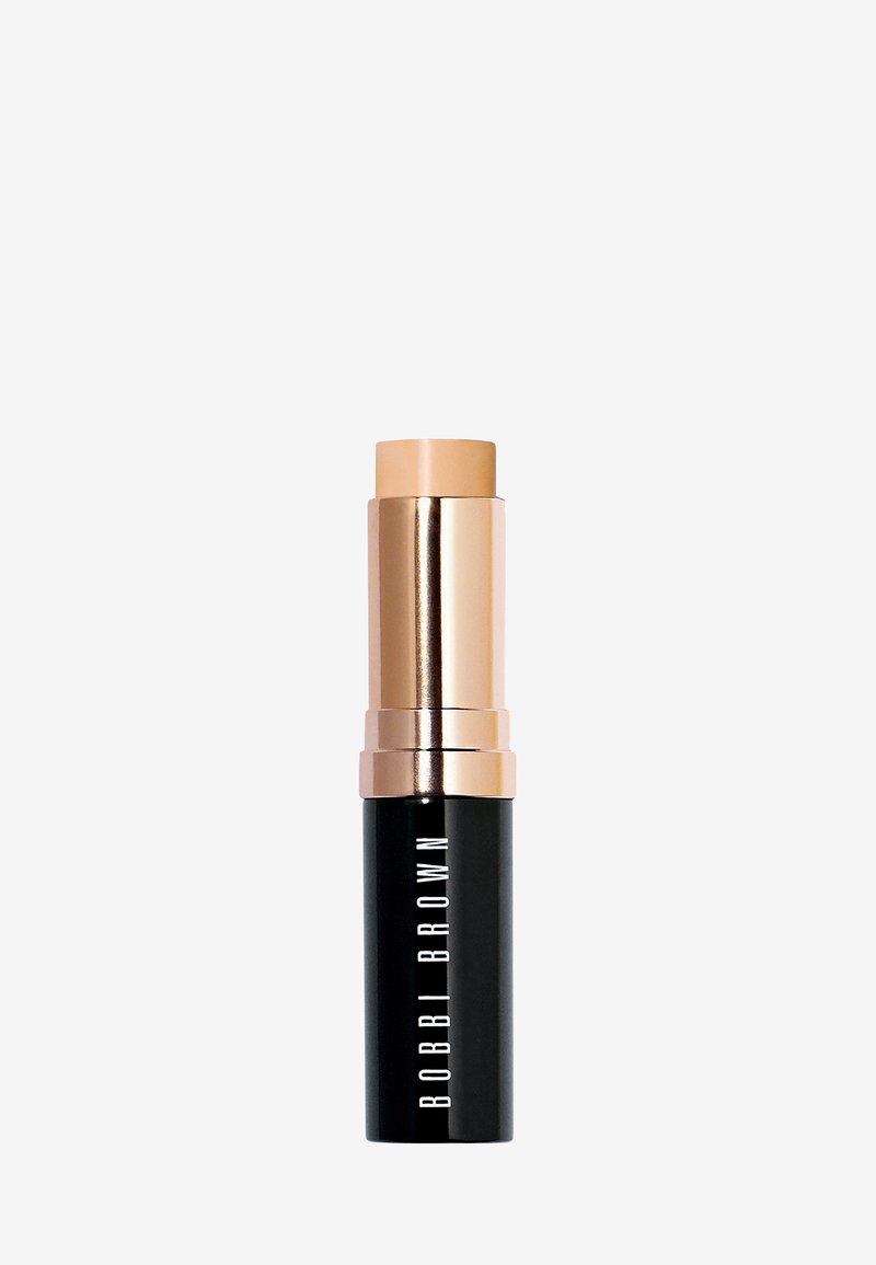 Stiftfoundation in een zwarte tube met gouden accenten. Heeft een romige, lichtbruine dop en de merknaam "BOBBI BROWN" in witte tekst.