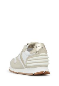 Der Sneaker verfügt über ein Obermaterial aus weißem Leder mit metallisch-goldenen Akzenten, Wildlederdetails und einer gepolsterten Sohle mit einer strukturierten braunen Außensohle.