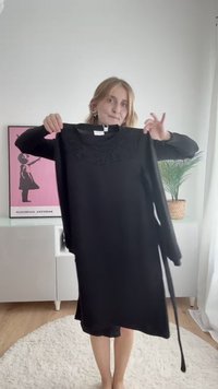 Juoda ilgomis rankovėmis suknelė, pasižyminti sudėtinga nėrinių detalėmis apykaklėje, laisvu siluetu ir nusagstomu juosmeniu. Glotni audinio tekstūra.