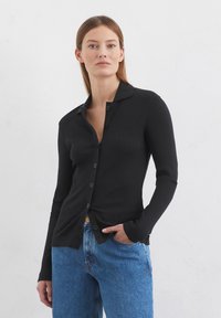 Schwarzes, geripptes Langarm- Hemd mit Knopfverschluss, das einen gekerbten Kragen und eine glatte Textur aufweist, kombiniert mit blauen Jeans.