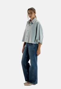 Lyseblå cropped jakke med bred krave og knaplukning, kombineret med højtaljede blå jeans og beige flade sko.