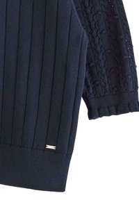 Maglione blu navy con design a coste sul corpo, maniche a rete e orlo texturizzato con un piccolo accento metallico.