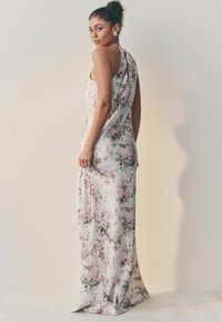 Lang blomsterklædning lavet af satin, med en hvid bund med pink og grønne blomster, en ærmeløs design og en flydende silhuet.