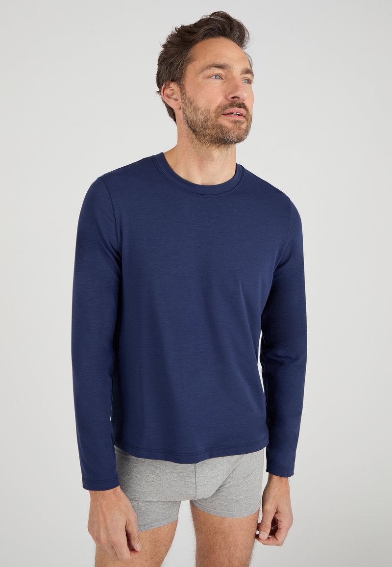 Maglietta a maniche lunghe blu navy in tessuto morbido con colletto girocollo, abbinata a pantaloni boxer grigi. Design semplice, vestibilità regolare, minimalismo nei dettagli.
