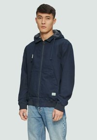 Sweat à capuche zippé bleu marine avec un cordon de serrage, poche kangourou à l'avant, bords côtelés aux manches et en bas, fabriqué à partir d'un mélange de coton.