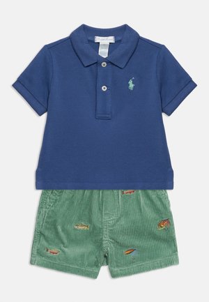 Navy blue short-sleeve polo shirt with green embroidered logo paired with green corduroy shorts featuring colorful fish embroidery.
