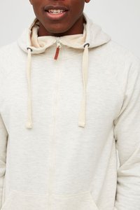 Svijetlosiva zip-up dukserica s bež akcentima, svezicom i prednjim džepom. Mekana tekstura i raglan rukavi za udobnost.
