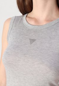 Canotta grigia in cotone con scollatura rotonda, caratterizzata da un piccolo dettaglio di design triangolare nella zona del petto. Tessuto liscio, design senza maniche.