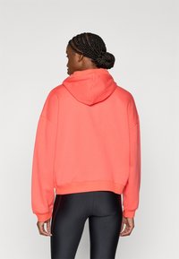 Κοραλλί cropped φούτερ με κουκούλα και κορδόνι, άνετη εφαρμογή και ριμπ μανσέτες. Συνδυάζεται με μαύρο κολάν, αναδεικνύοντας μια μίνιμαλ σχεδίαση.