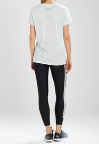 Maglietta sportiva azzurra chiara con maniche corte, abbinata a leggings neri con una striscia grigia lungo il lato e scarpe da corsa scure.