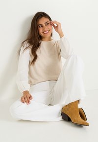 Top de punto beige con largas mangas blancas texturizadas, combinado con pantalones anchos blancos y botas de tacón de gamuza mostaza. Atuendo sencillo y casual.
