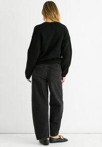Black knitted sweater with a relaxed fit, ribbed hem, paired with wide-leg black jeans, and black flats. Visible back stitching details.