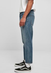 Light blue denim jeans with a straight-leg cut, featuring five pockets and a worn-in texture. Paired with black and white sneakers.