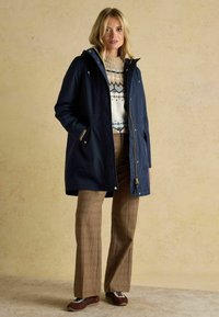 Námornícky vodotesný parka s zipsom a kapucňou, s kovovými prvkami v zlatej farbe. Skombinované s pleteným sveterom a kockovanými rozšírenými nohavicami.