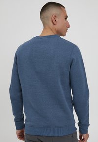 Kék pulóver kerek nyakkal, hosszú ujjal, bordázott mandzsettával és szegéllyel. Puha anyagból készült, sima textúrával.