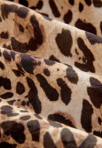 Lepardskinprint stof met een gladde textuur, met een beige achtergrond en donkerbruine vlekken van verschillende groottes en vormen.