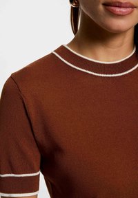 Top in maglia marrone con un design aderente. Presenta un collo rotondo e polsini a righe bianche. Texture liscia, maniche corte e senza motivi visibili.