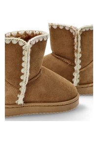 Botas de tobillo de ante marrón con costuras decorativas blancas a lo largo del borde superior y una suela de goma texturizada. Diseño de punta redonda para mayor comodidad.