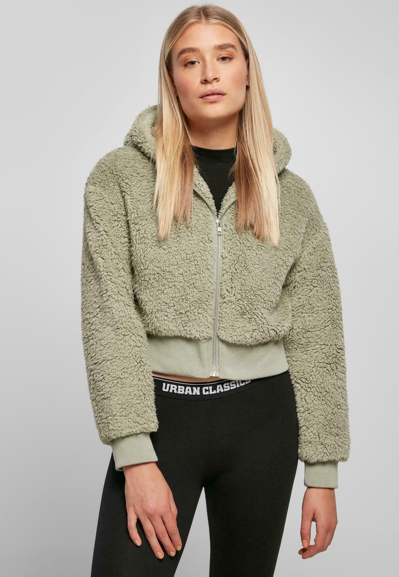 Korte zip-up hoodie in lichtgroen, gemaakt van een fuzzy materiaal. Voorzien van een capuchon en elastische manchetten, gecombineerd met zwarte leggings met het merklogo.