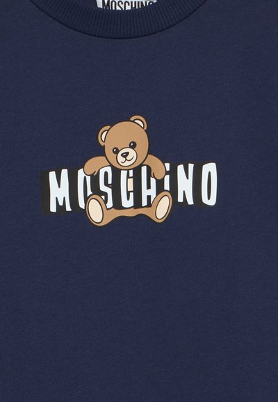 Tissu bleu marine avec un ours en peluche tenant des lettres blanches en blocs formant le mot « MOSCHINO » sur son corps.
