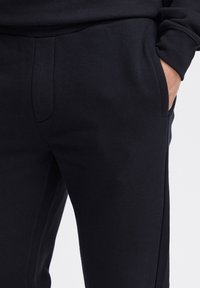 Tamsiai mėlynos jogger stiliaus kelnės, pagamintos iš minkšto medvilnės mišinio. Yra šoninės kišenės ir lygi, tekstūruota paviršiaus bei prigludusio dizaino.