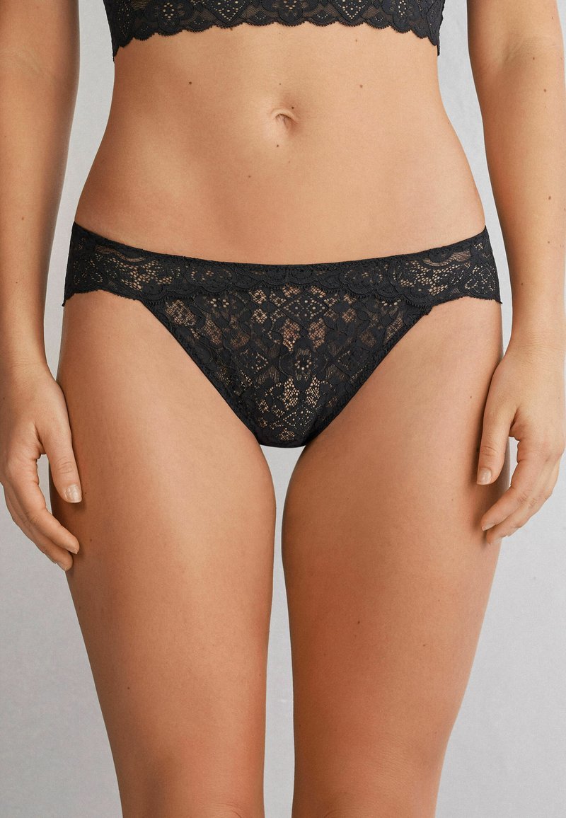 Schwarze Spitzen-Bikini-Unterhosen mit floralen Mustern, gewellten Kanten und einer weichen Textur. Entworfen für Komfort und eine figurbetonte Silhouette.