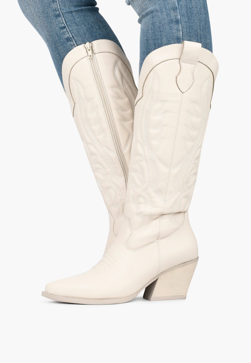 Botas de cowboy de cuero blanco con costuras decorativas, puntera ligeramente afilada y tacón apilado. Cierre de cremallera en el costado.