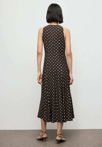 Vestido marrón sin mangas con lunares blancos, falda acampanada, a la altura de la rodilla, hecho de una tela suave, con una textura lisa y una silueta ajustada.