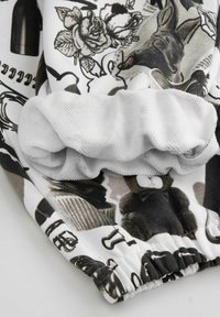 Czarno-biała tkanina z kwiatowymi i zwierzęcymi nadrukami, z teksturowanym białym elastycznym mankietem do regulowanego dopasowania.