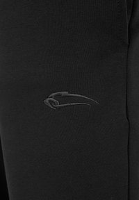 Zwarte sportbroek met een strakke pasvorm, gemaakt van zachte, rekbare stof. Heeft een subtiele, reliëf logo op de bovenkant van het bovenbeen.