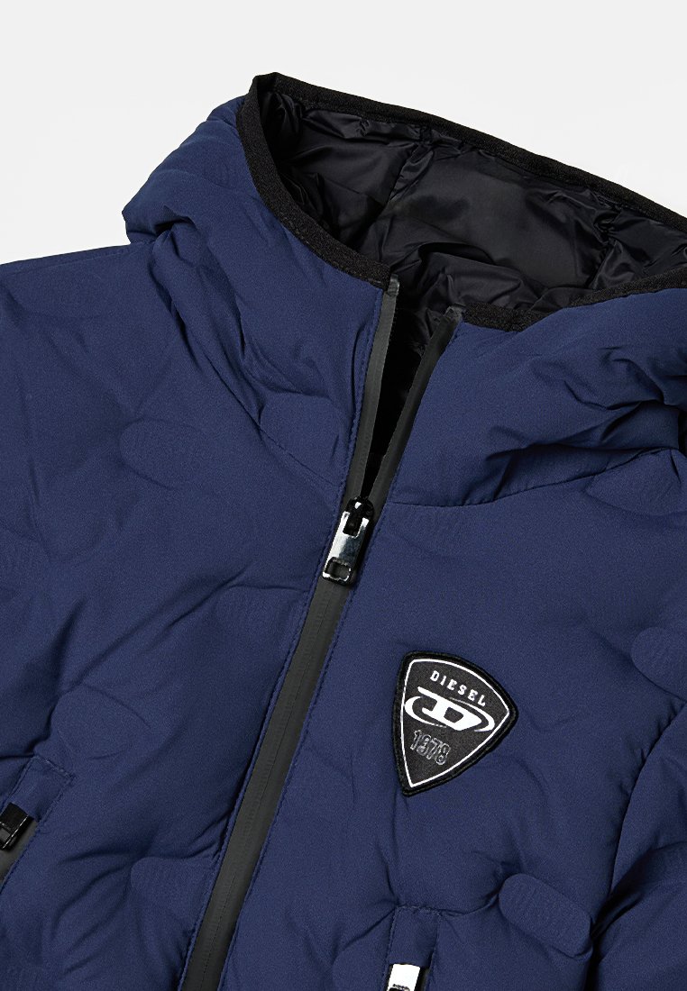 Marineblaue Steppjacke mit einem schwarzen Logopatch, Reißverschluss, strukturiertem Muster, glattem Innenfutter und elastischer Kapuze.
