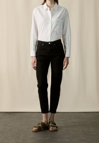 Vit långärmad skjorta med ficka, tillsammans med svarta skinny jeans och bruna sandaler med remmar. Enkelt mönster, slät textur och neutrala färger.