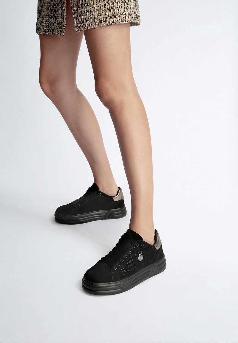 Černé tenisky vyrobené z nubuku a plátna, s texturovaným svrškem, šněrováním a kontrastním stříbrným akcentem na patě.