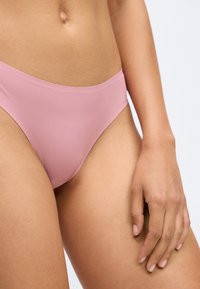 Helle rosa Bikini-Brief mit glatter Textur, minimalistischem Design und niedrigem Schnitt, der den Oberschenkelbereich und die Taille betont.