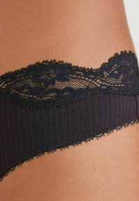 Zwart ondergoed met kantafwerking, voorzien van een geribbelde textuur en golvende randen, met fijne details langs de tailleband.
