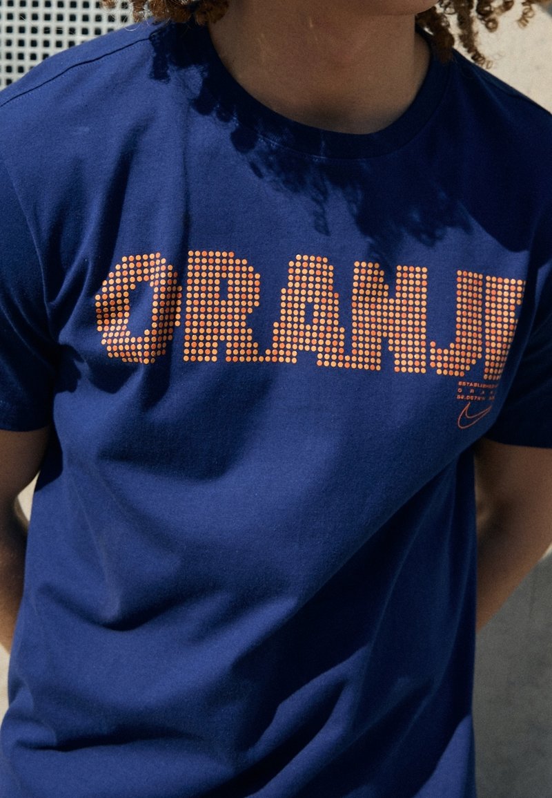 T-shirt en coton bleu marine avec le texte "ORANJE" en pointillés orange sur la poitrine ; design simple avec col rond et manches courtes.