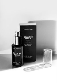 Black glass serum bottle with silver pump, labeled “Cellular Repair Serum.” Accompanied by a black box and clear cap. Minimalist design.
