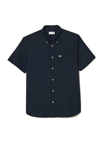 Chemise à manches courtes bleu marine avec un col classique, une poche poitrine et un petit logo crocodile vert. Texture de tissu lisse.