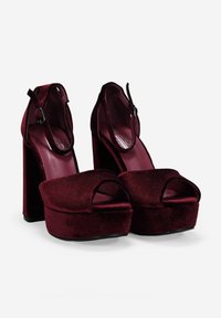 Zapatos de plataforma de terciopelo burdeos de tacón alto con un diseño de punta abierta, correa en el tobillo y un grueso tacón cuadrado. Textura suave con acentos mínimos.