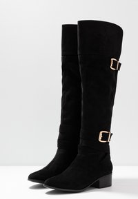 Botas altas de imitación de ante negras hasta la rodilla con punta afilada, tacón block y hebillas doradas en las correas cerca de la parte superior y a mitad de pantorrilla.
