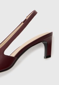 Sandal con tacco medio in pelle bordeaux con soletta imbottita beige su sfondo bianco.