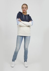 Hettegenser med marineblå kropp, lyseblå ermer og kremfarget nedre del; med en frontlomme og hvite snorer. Kombinert med lyseblå jeans og hvite joggesko.