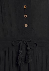 Vestido negro con textura vertical, detalles de botones de madera y un cinturón atado con borlas en la cintura. Diseño sencillo y funcional.